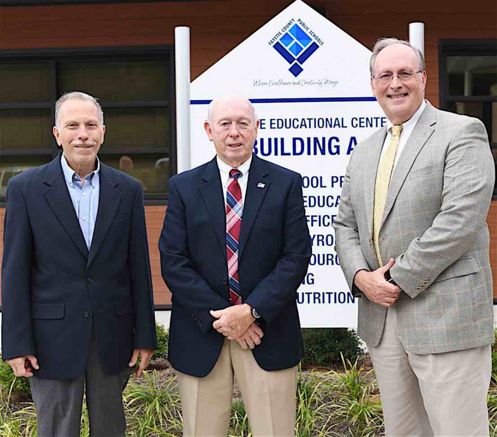 Former Fayette County Public School superintendents Dr. John DeCotis and Trigg Dalrymple take their place alongside current Fayette County Public School Superintendent Dr. Joseph Barrow in front of the school system’s new logo. Photo/Fayette School System.