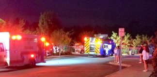 Emergency vehicles are watched by spectators in front of the NCG Theater just west of Peachtree City. The car went through a fence into a stormwater retention pond. Photo/Deb Drake.