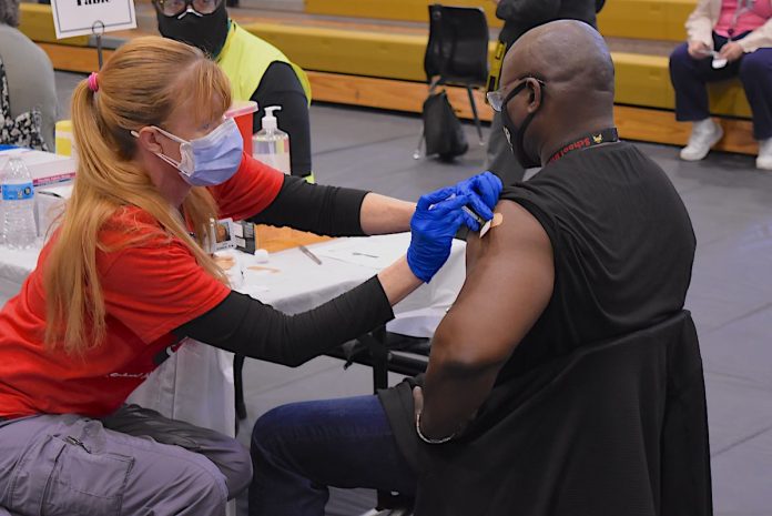 A Fayette County School System nurse injects an employee with the first dose of the Covid-19 vaccine at one of 30 stations on the floor of Fayette County High School Gymnasium March 11. Photo/Cal Beverly.