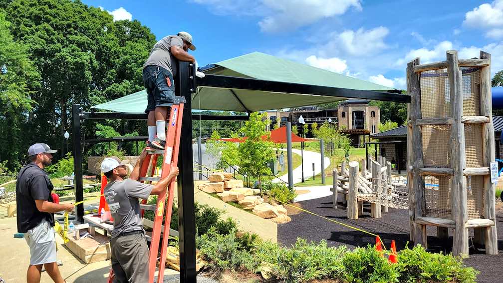 Workers install sunshade over popular hillside slide in Fayetteville City Center Park.