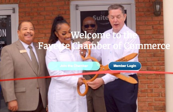 Fayette Chamber of Commerce President Colin Martin (at right, holding scissors) helps cut the ribbon opening a new business. Fayetteville Mayor Ed Johnson is at left. Photo/Fayette Chamber website.